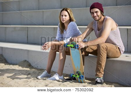 young couple of skateboarders, sitting on concrete steps, talking  on the beach, on a beautiful summer day.
