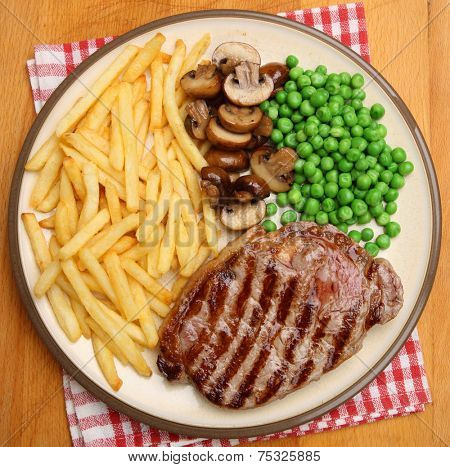 Chargrilled sirloin steak dinner with fries, mushrooms and peas.