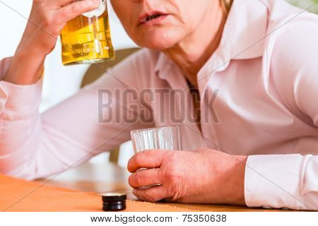 Old woman with alcohol problem sitting at home drinking hard liquor 
