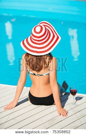 Back shot of young woman sitting close by swimming pool