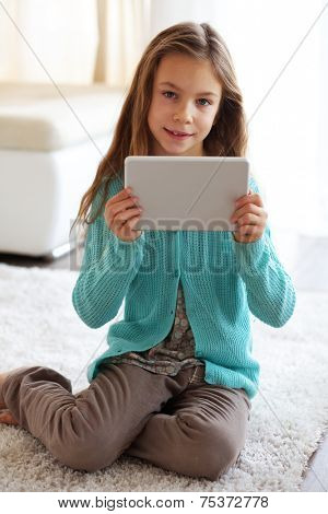 Child playing on ipad tablet pc sitting on a carpet at home