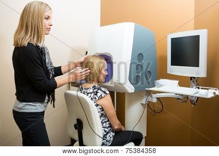 Female optometrist adjusting patient's head while looking at computer for retinal checkup