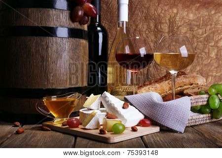 Supper consisting of Camembert and Brie cheese, wine and grapes on cutting board and wine barrel on wooden table on brown background