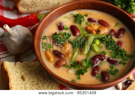 Bean soup in bowl with fresh sliced bread on napkin, on wooden table background