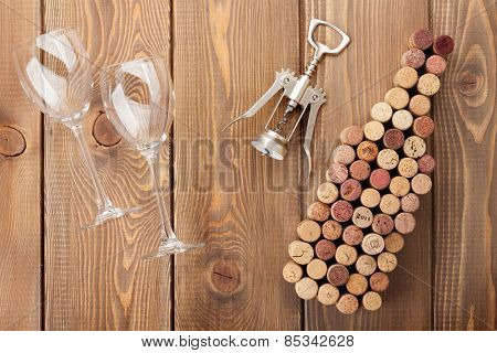 Wine bottle shaped corks, glasses and corkscrew over rustic wooden table background. View from above