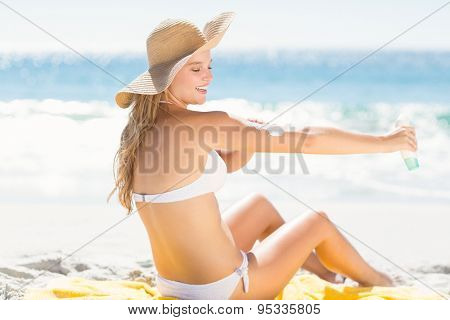 Pretty blonde woman spreading sun tan lotion on her arms at the beach