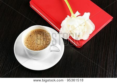 Cup of coffee with notebook and fresh flower on wooden table background