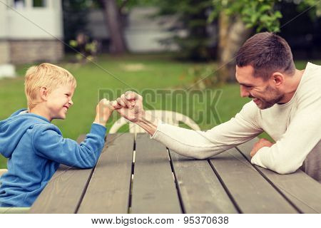family, happiness, generation, home and people concept - happy father and son doing arm wrestling outdoors