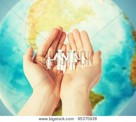 people, population, charity and life concept - close up of human hands holding paper family over earth globe and blue background