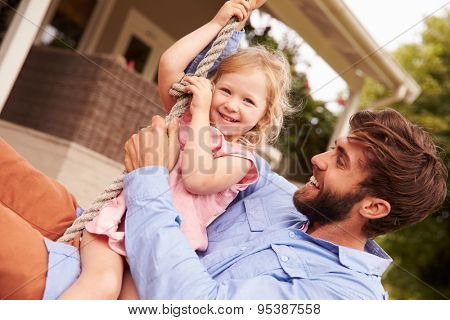 Father playing with daughter on a rope swing in a garden