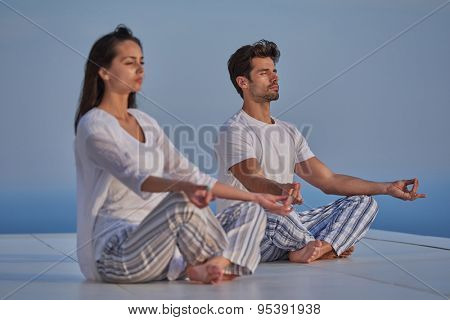 young couple practicing yoga at sunset in modern home terace with ocean and sunset in background