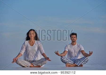 young couple practicing yoga at sunset in modern home terace with ocean and sunset in background