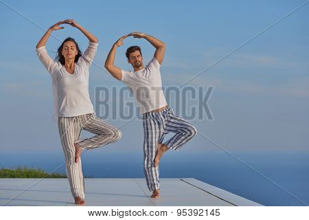 young couple practicing yoga at sunset in modern home terace with ocean and sunset in background