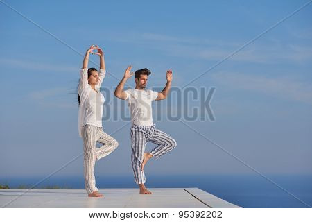 young couple practicing yoga at sunset in modern home terace with ocean and sunset in background