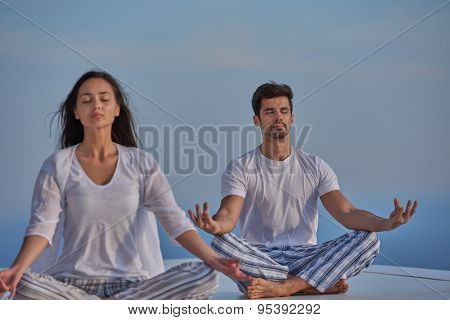 young couple practicing yoga at sunset in modern home terace with ocean and sunset in background