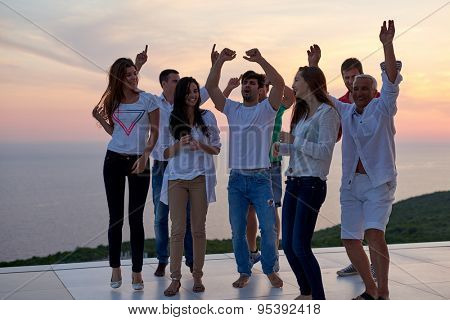 group of happy young people dancing and have fun on party in modern home bacony with sunset and ocean in background