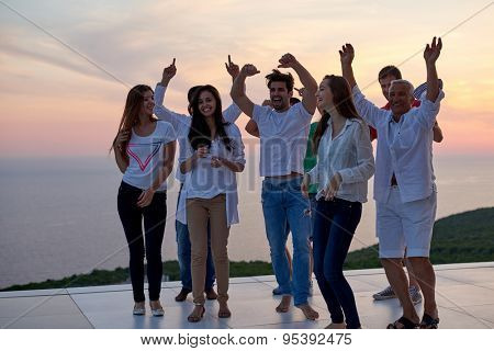 group of happy young people dancing and have fun on party in modern home bacony with sunset and ocean in background