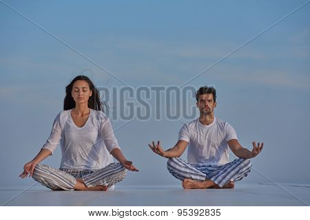young couple practicing yoga at sunset in modern home terace with ocean and sunset in background