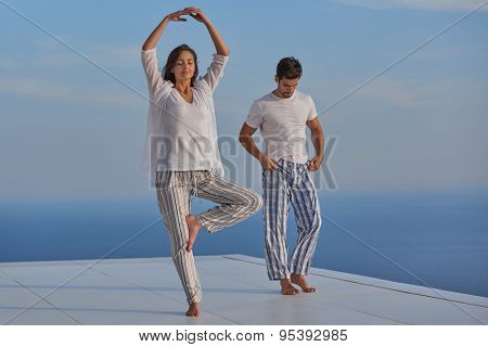 young couple practicing yoga at sunset in modern home terace with ocean and sunset in background
