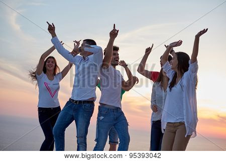 group of happy young people dancing and have fun on party in modern home bacony with sunset and ocean in background
