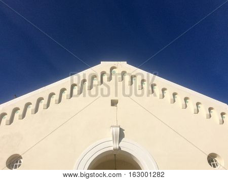 Looking up at scalloped roof trim of a historic cream stucco building with architectural details against a backdrop of a dark blue sky