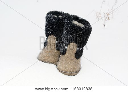 Russian traditional winter felt gray kids boots valenki with fur standing on the snow. Snow poured shoes.