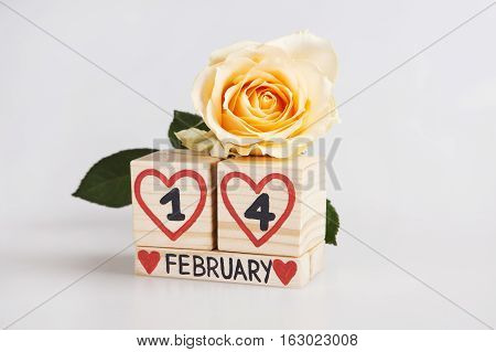 Valentine's day composition with wooden calendar and yellow rose. Handwritten February 14th inside red hearts. Bright background.