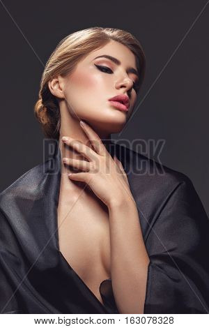 Portrait of beautiful young woman with cat eye make-up in black fabric. Studio beauty shot over black background.