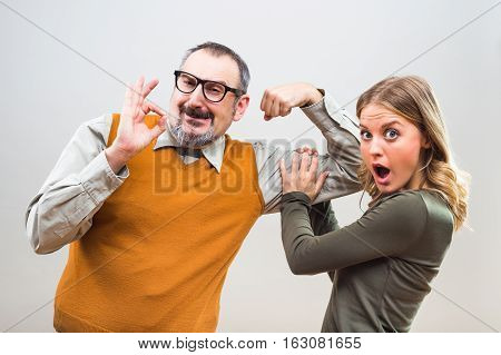 Nerdy man is showing to a beautiful woman how strong he is and she is impressed.