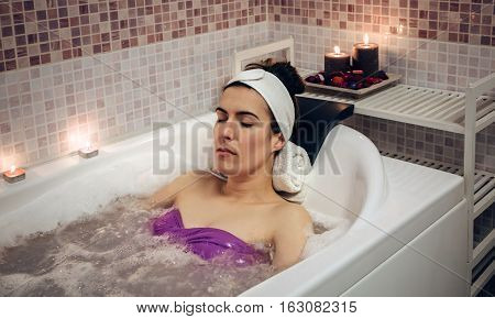 Beautiful woman with closed eyes lying in tub doing hydrotherapy treatment. Health and beauty concept.