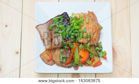 Trout in marinade with vegetables on a white plate. Background light tree