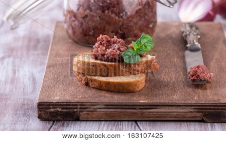 Red onion chutney in a glass jar and toasts with chutney on old wooden cutting board. Rustic table-knife.