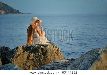 Young woman with hat sits back on the sea stone
