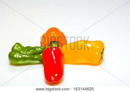 Green redyellow and orange peppers lined up against a bright white background