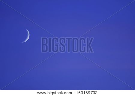 Rising crescent moon in blueish evening sky.