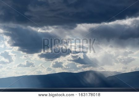 Dark gray dramatic sky with large clouds above the lake against black mountains. Lake Baikal.