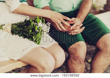 Cropped shot of young couple holding hands while sitting together outdoor. Focus on hands.