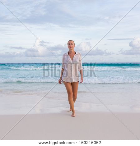 Woman wearing white loose tunic over bikini on Mahe Island, Seychelles. Summer vacations on picture perfect tropical beach concept.