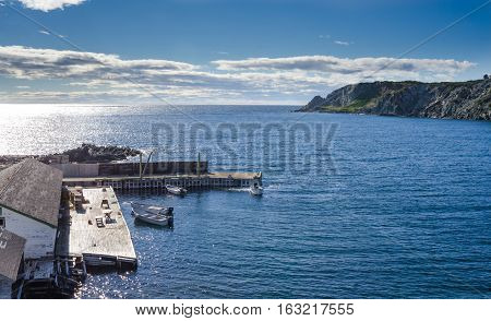 boats at a cliff-side dock house in Twillingate, Newfoundland, man works on the engine of one of 4 boats tied up to a wooden, cliff-side dock house for the day,