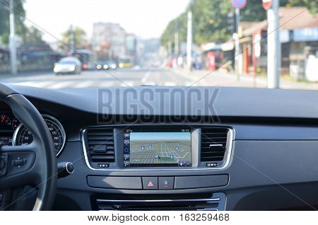 View from inside a car on a part of dashboard with a navigation unit and blurred street in front of a car