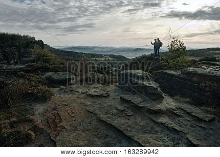 two young people photographing rocks in the czech tourist area Tiske skaly in winter without snow at dawn