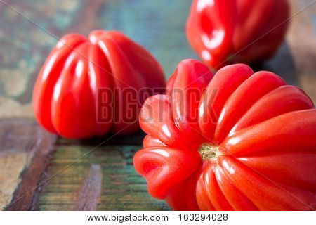 Close up of three red oxheart tomatoes on a wooden table