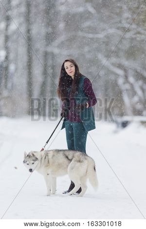 Portrait of Lovely Caucasian Brunette Woman Along With Her Husky Dog. Walking Together Outdoors in Snowy Winter Forest.Vertical Image composition