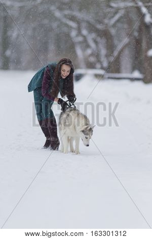 Young Caucasian Brunette Girl Walking With Husky Dog Outside in Winter Snowy Forest.Vertical Image Orientation
