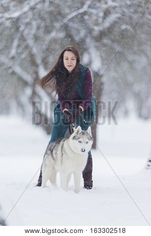 Happy Smiling Caucasian Brunette Woman and Her Husky Dog. Playing Outdoors in Winter White Forest Together. Vertical Image