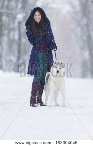 Positive Caucasian Woman Airing Her Husky Dog. Walking In Winter Forest Outdoors.Vertical Image Composition