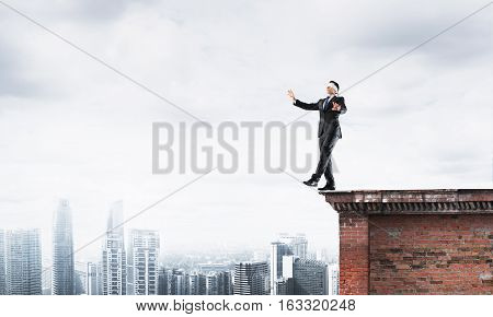 Businessman with blindfolder on eyes walking on building top