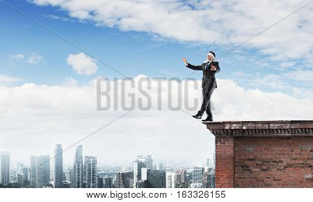 Businessman with blindfolder on eyes walking on building top