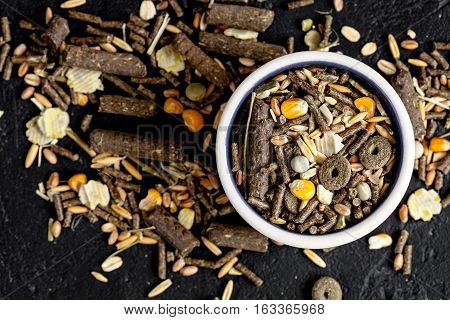 dry food for rodents in bowl on dark background top view.