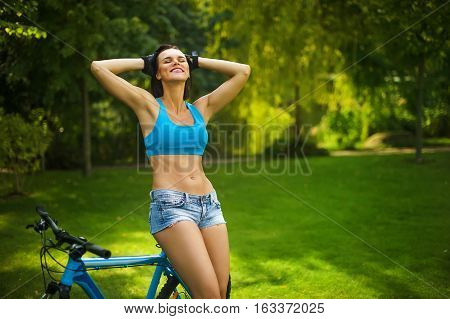 a woman stands on the grass in a Park with a bike and enjoys the summer sun